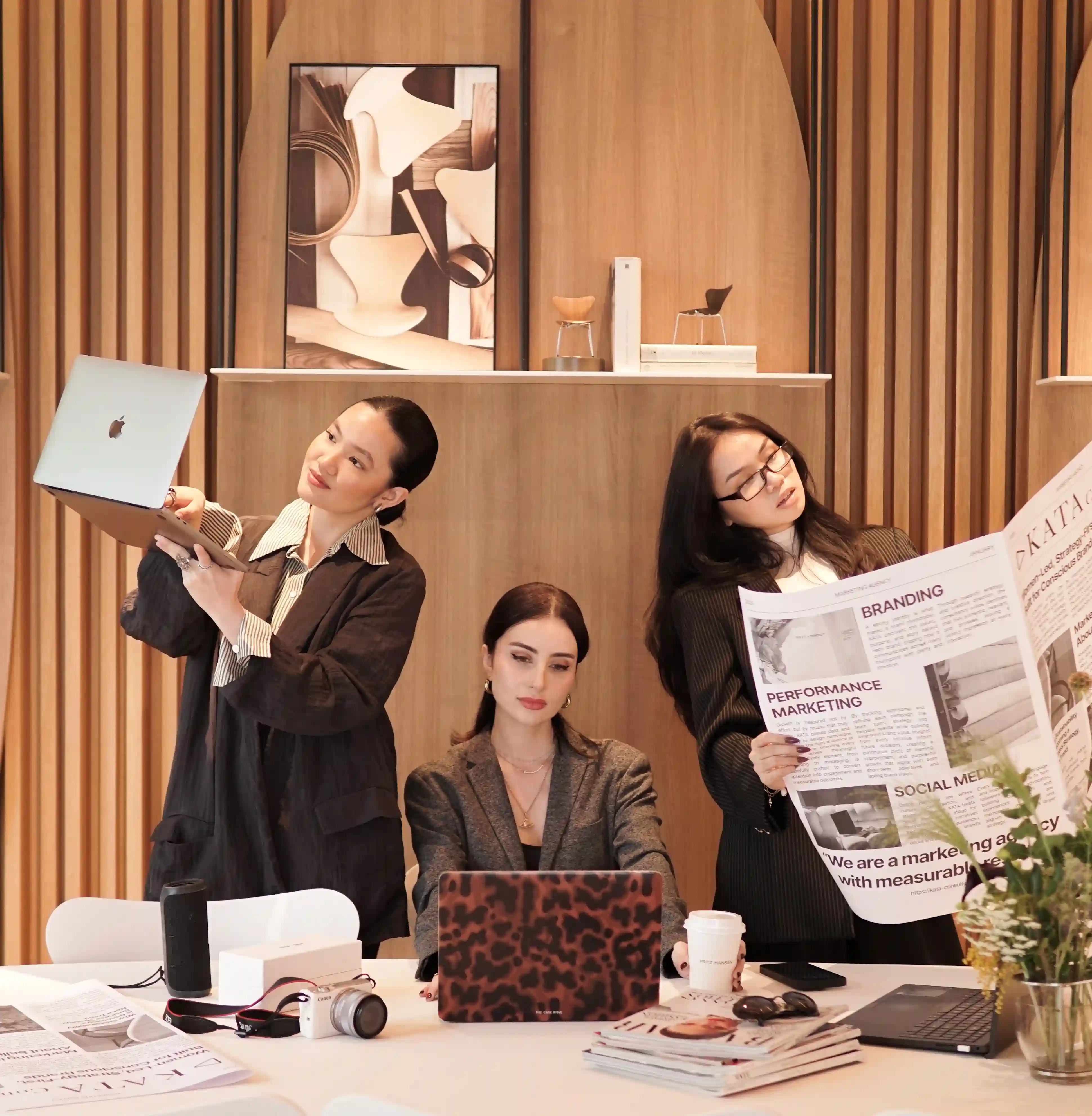 Three KATA team members standing together, one holding a laptop with a leopard-print case